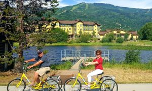 Residents bike past Caseys Pond with Steamboat Springs in the background